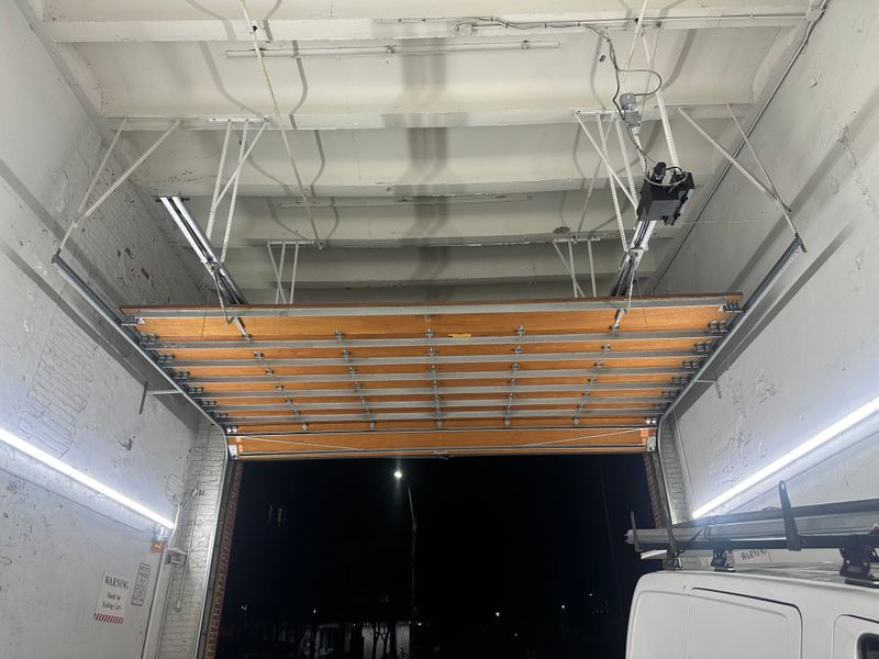 Commercial wood overhead door open at night showing interior with van and track system — MA